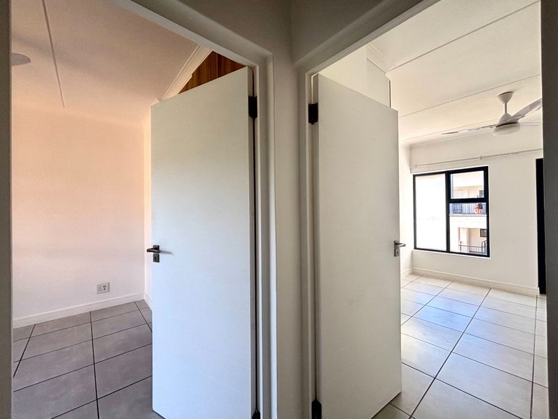 A bright hallway featuring tiled flooring and access to two separate rooms, showcasing clean finishes and modern internal doors.