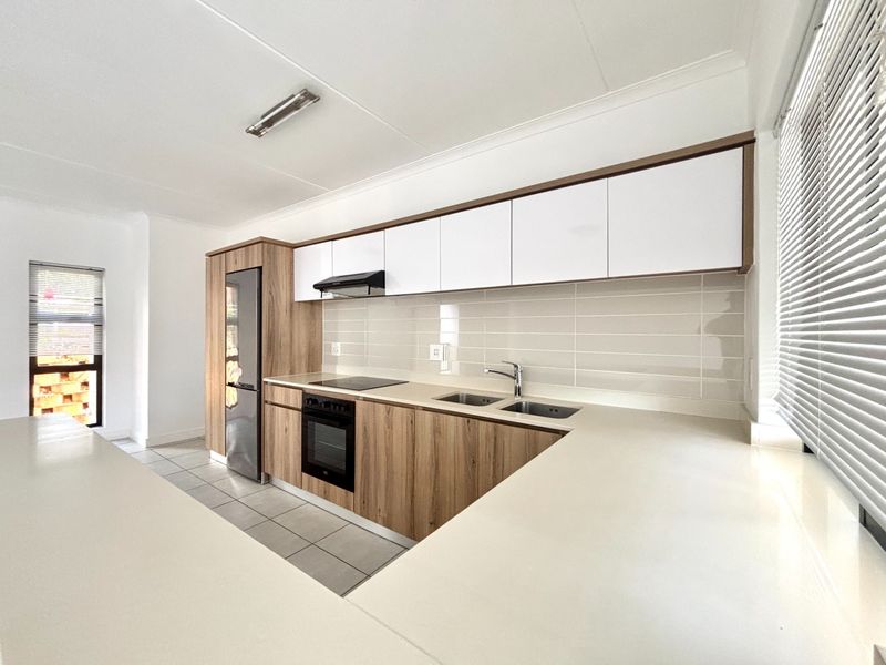 Modern kitchen featuring wood-grain and white cabinetry, stone countertops, integrated appliances, and a clean subway tile backsplash in a bright, open-plan layout.