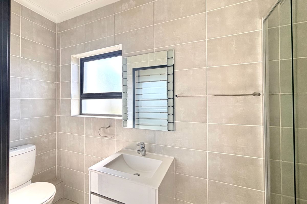 Modern bathroom featuring neutral wall tiles, a vanity cabinet with integrated basin, a glass shower enclosure, and a wall-mounted mirror.