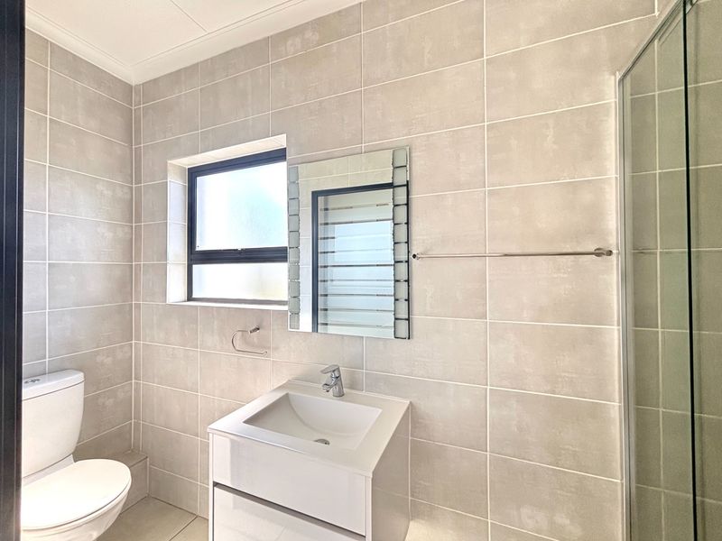 Modern bathroom featuring neutral wall tiles, a vanity cabinet with integrated basin, a glass shower enclosure, and a wall-mounted mirror.