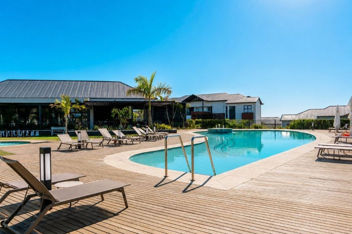 A well-maintained outdoor swimming pool area featuring timber decking, a water feature, and surrounding communal facilities.