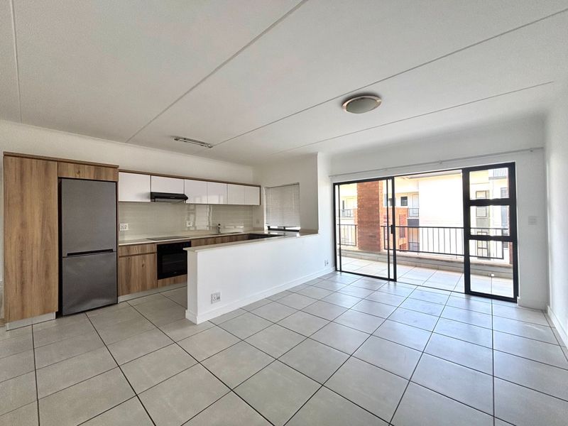 Modern open-plan kitchen and living area featuring tiled floors, built-in cabinetry, and direct access to a private balcony through sliding glass doors.