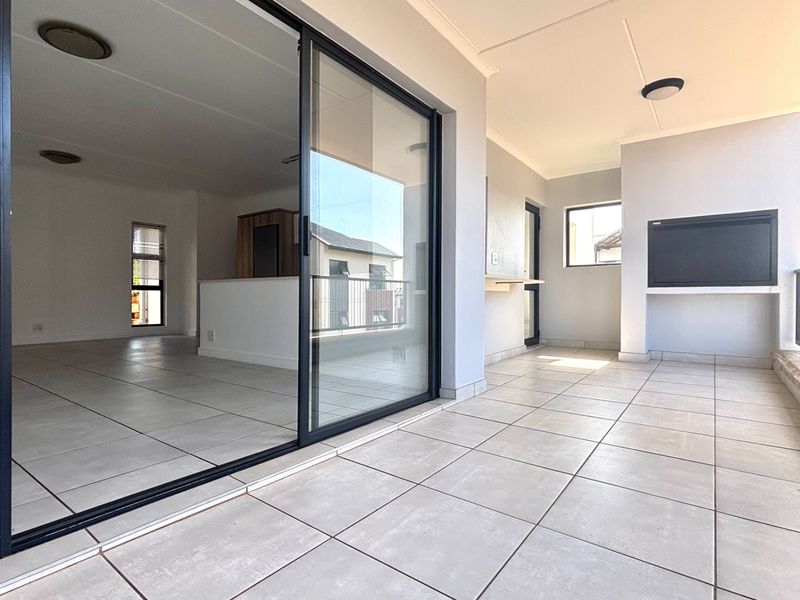 A spacious covered balcony featuring tiled flooring, a built-in braai, and large sliding glass doors providing seamless access to the interior living area.