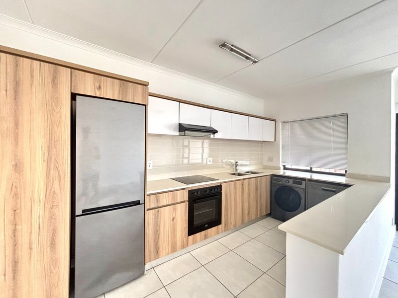 Modern kitchen featuring light wood-grain cabinetry, stone countertops, integrated appliances, and tiled flooring in a clean, functional layout.