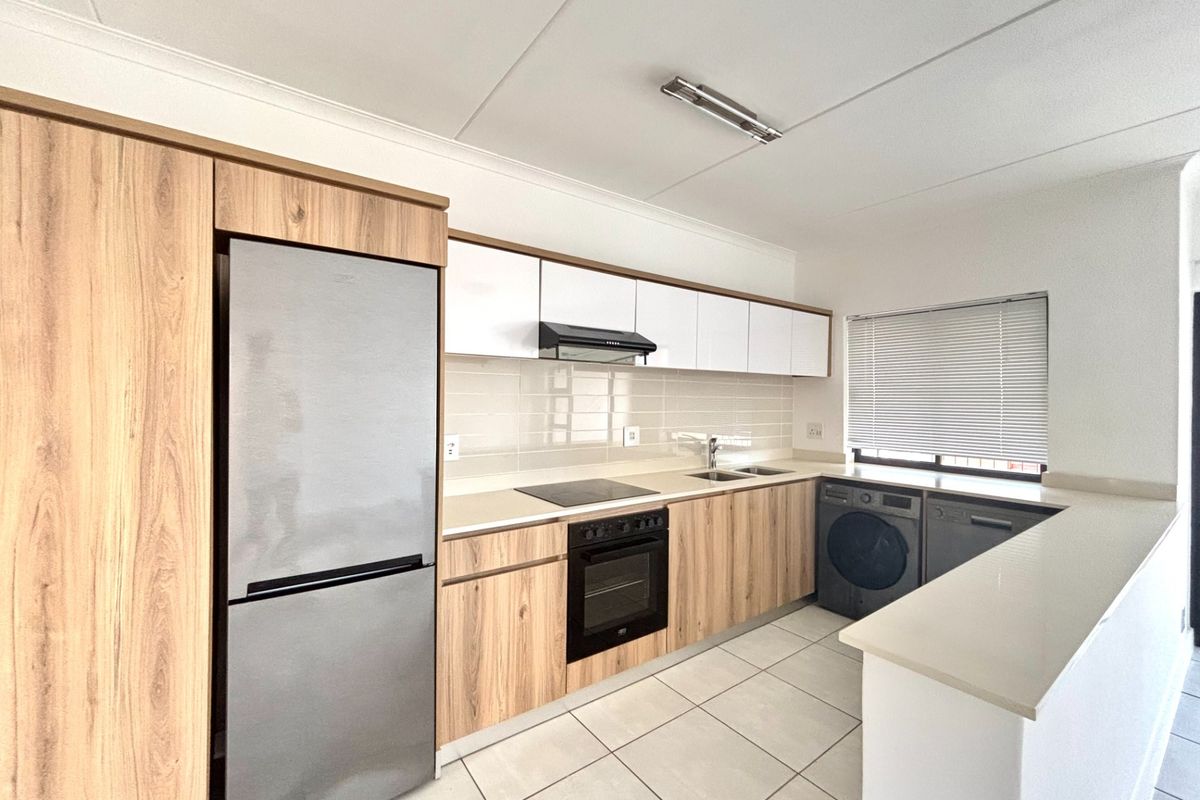 Modern kitchen featuring light wood-grain cabinetry, stone countertops, integrated appliances, and tiled flooring in a clean, functional layout.