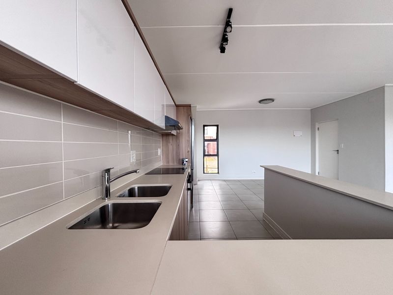Modern open-plan kitchen and living area featuring sleek cabinetry, integrated hob, double sink, and neutral tiled flooring in a clean, contemporary space.