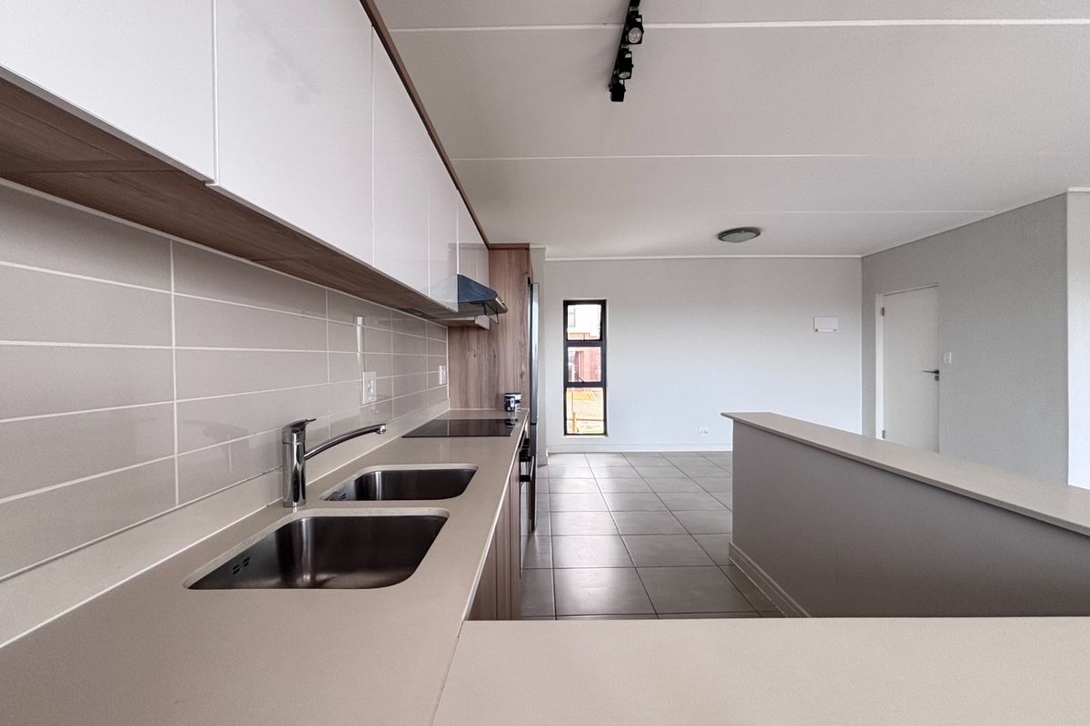Modern open-plan kitchen and living area featuring sleek cabinetry, integrated hob, double sink, and neutral tiled flooring in a clean, contemporary space.