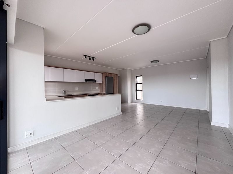 A bright, open-plan living and kitchen area featuring modern cabinetry, tiled flooring, and neutral finishes, providing a versatile space for living and dining.