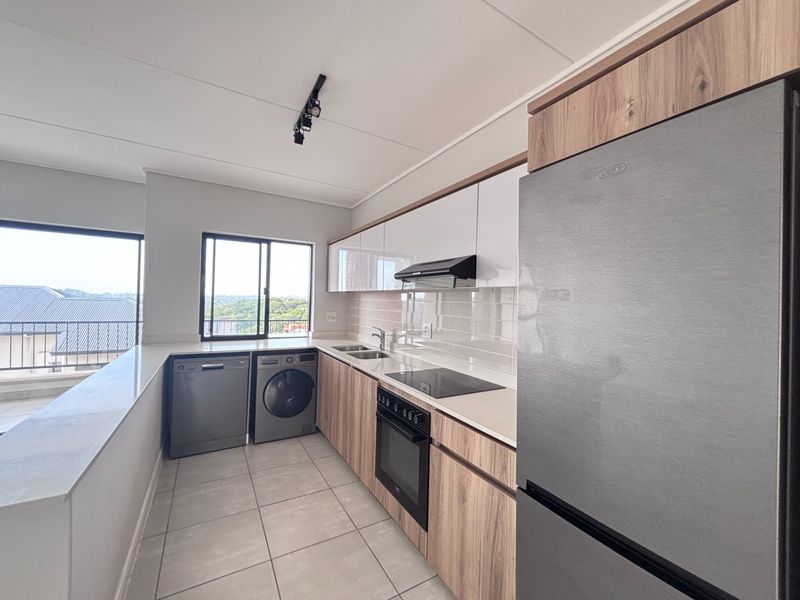 Modern kitchen featuring sleek wood-grain and white cabinetry, stone countertops, integrated appliances, and tiled flooring with ample natural light.