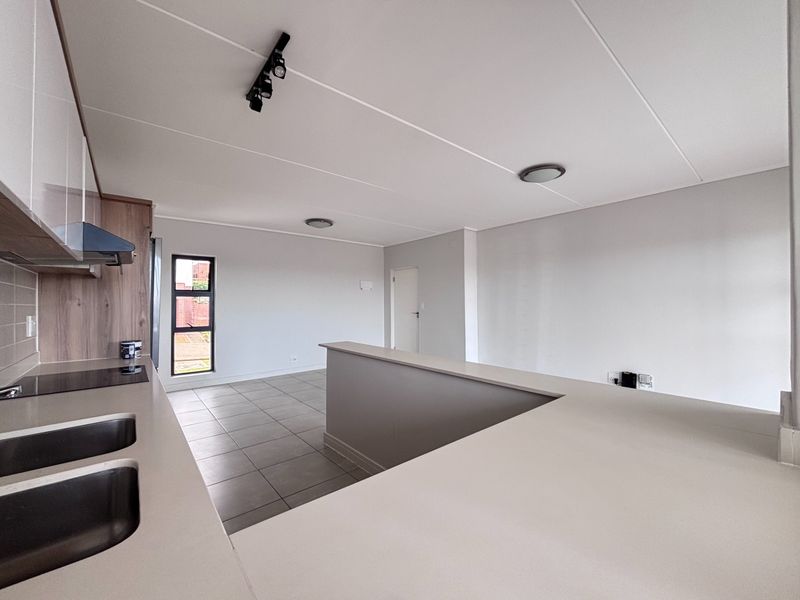 Modern open-plan kitchen and living area featuring neutral tiled flooring, sleek cabinetry, and a functional breakfast bar, offering a bright and versatile living space.