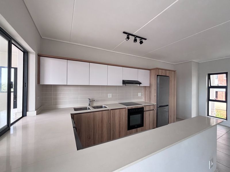 Modern kitchen featuring sleek wood-tone and white cabinetry, stone countertops, integrated appliances, and a functional breakfast bar layout.