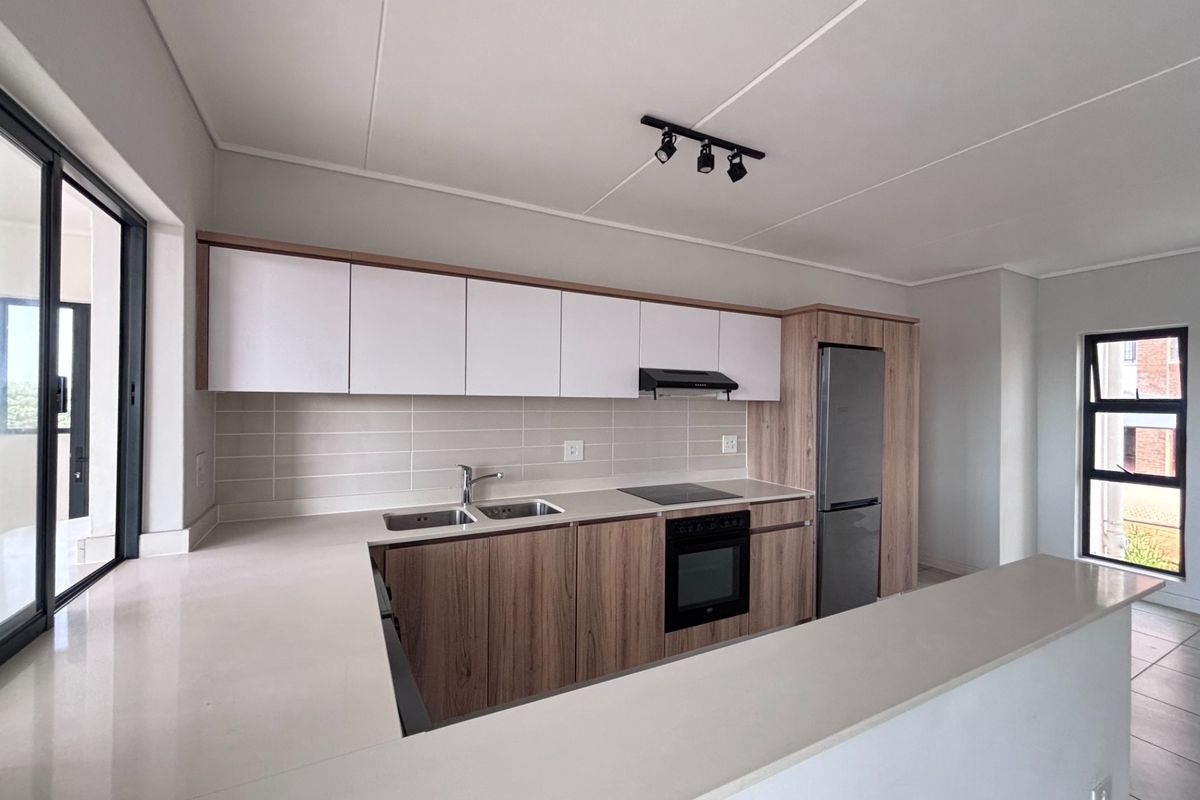 Modern kitchen featuring sleek wood-tone and white cabinetry, stone countertops, integrated appliances, and a functional breakfast bar layout.