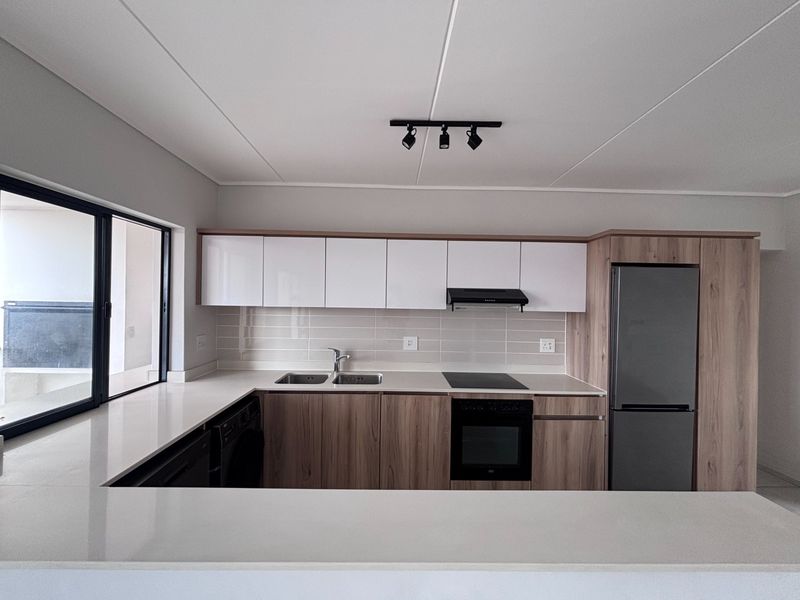 Modern kitchen featuring sleek wood-tone and white cabinetry, stone countertops, integrated appliances, and a functional layout with a breakfast bar.