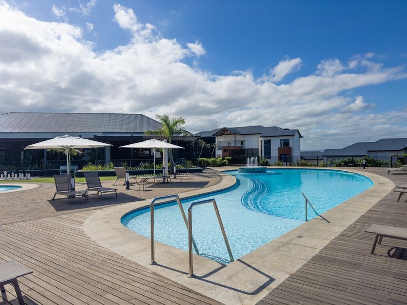 A well-maintained communal swimming pool area featuring timber decking, a central fountain, and paved surrounds within a residential apartment complex.