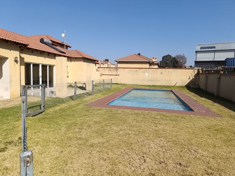 A private backyard area featuring a swimming pool with paved surround, enclosed by perimeter walls and wire fencing.