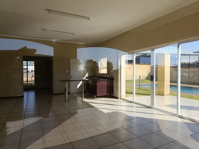 Spacious open-plan living area featuring tiled floors, a small built-in kitchenette, and large sliding glass doors opening to an outdoor pool area.