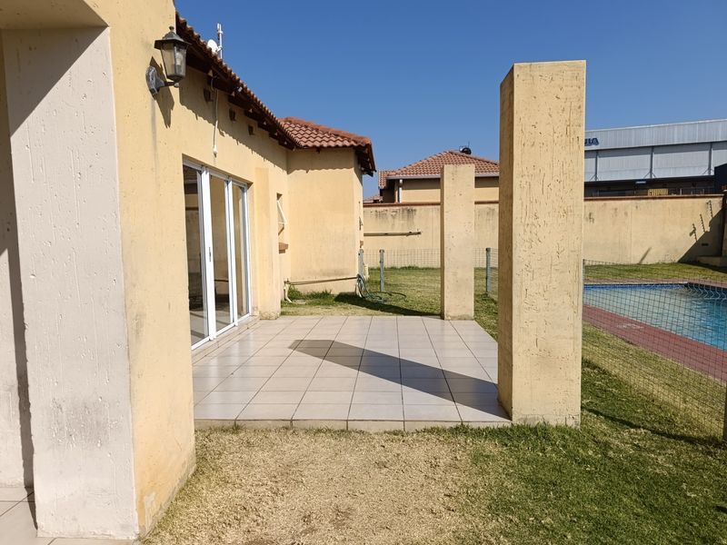 A covered patio area featuring tiled flooring and concrete pillars, providing direct access to the garden and swimming pool area.