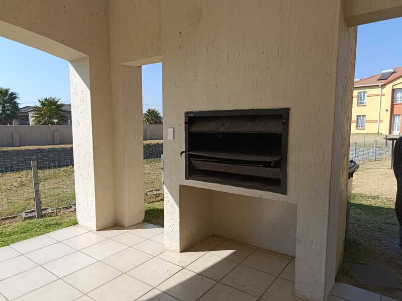 Covered patio area featuring a built-in braai and tiled flooring, offering an open outdoor space suitable for entertainment.