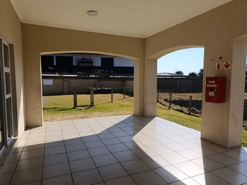 A covered patio area featuring tiled flooring, arched structural pillars, and a wall-mounted fire extinguisher cabinet, overlooking an open outdoor space.