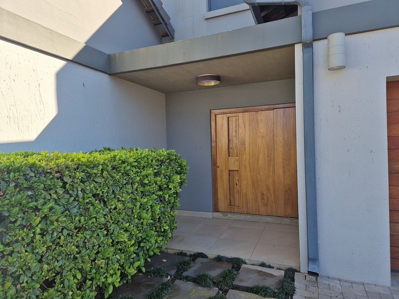 A welcoming front entrance featuring a solid wood door, tiled porch area, and modern exterior lighting under a concrete roof overhang.