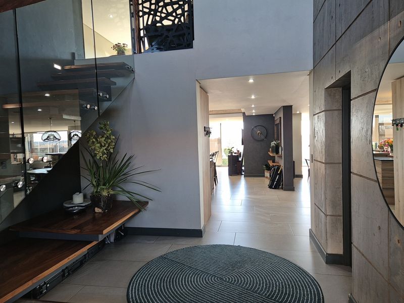 Modern entrance hall featuring a striking floating timber staircase with glass balustrade, tiled flooring, and contemporary concrete wall finishes leading into the open-plan living area.