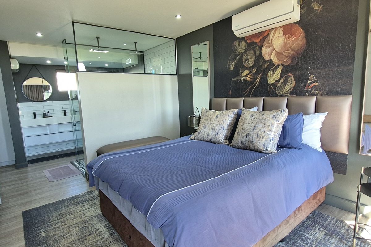 Modern bedroom featuring an open-plan ensuite with a glass partition, walk-in shower, double vanity, and integrated split-system air conditioning.
