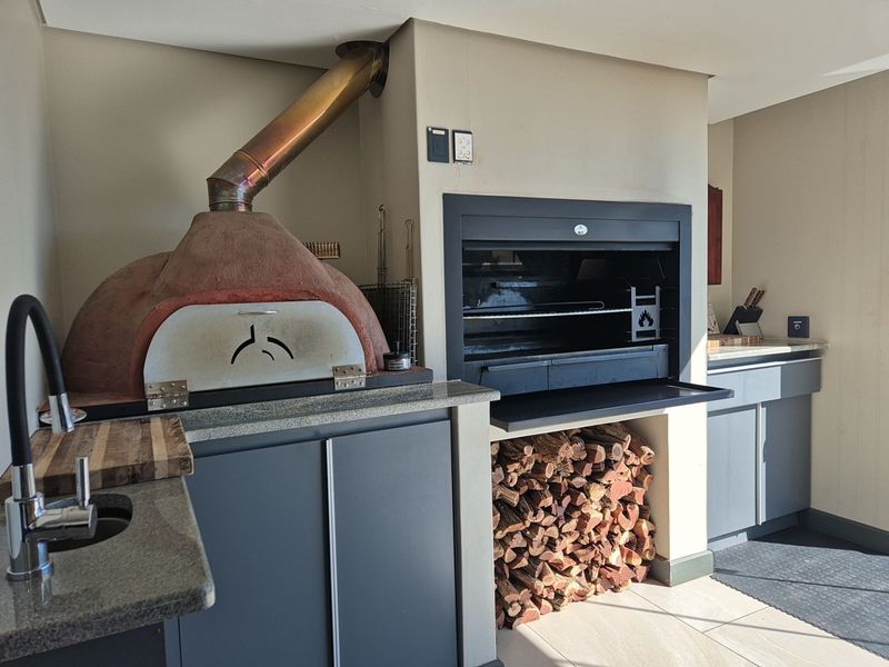 Outdoor entertainment area featuring a built-in pizza oven, integrated braai, granite countertops, and ample storage cabinetry.