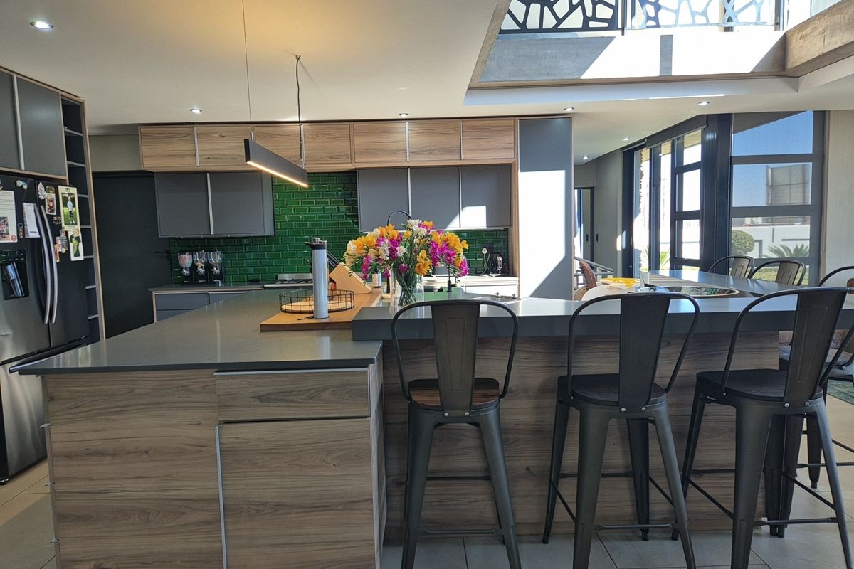 Modern kitchen featuring a large island with stone countertops, wood-grain cabinetry, green subway tile backsplash, and a bright skylight overhead.