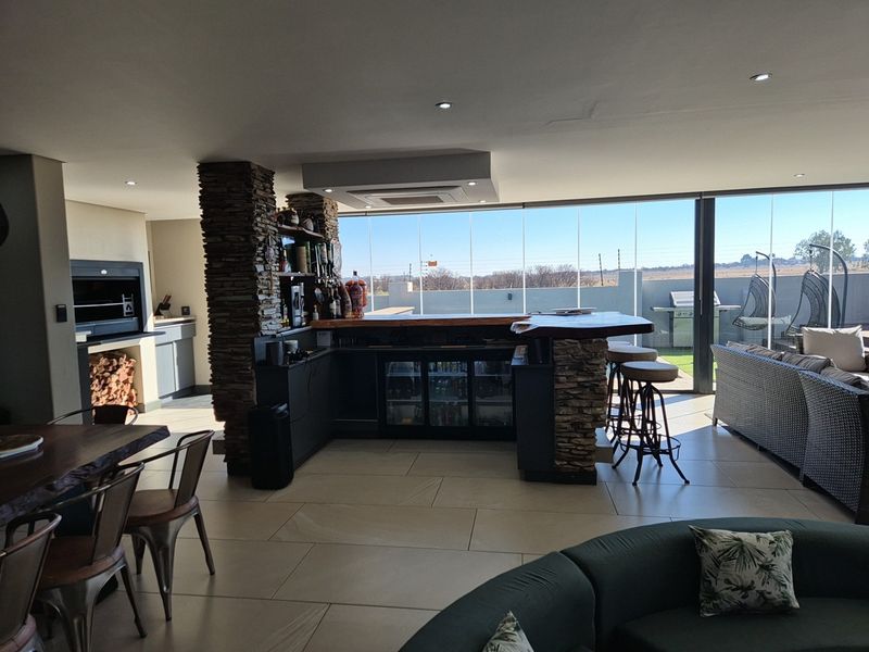 Spacious open-plan entertainment area featuring a built-in braai, stone-clad bar with integrated refrigeration, and large stacking glass doors opening to the outdoors.