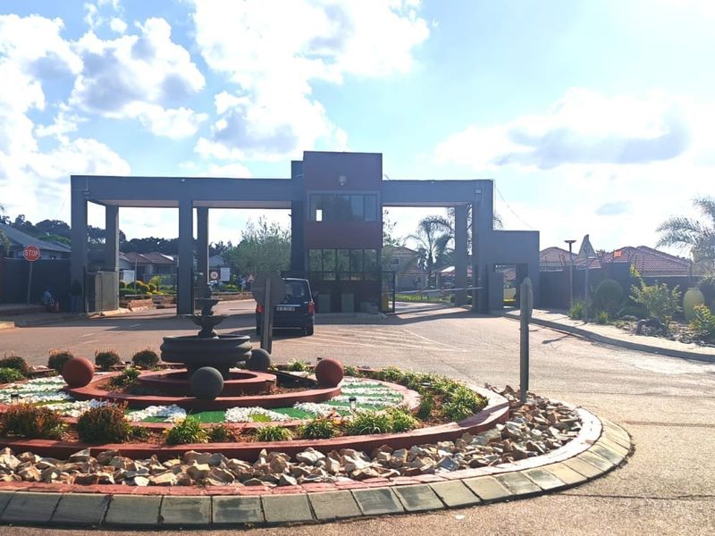 The entrance to the residential estate features a secure gatehouse, boom gate access, and a landscaped roundabout with a central fountain.