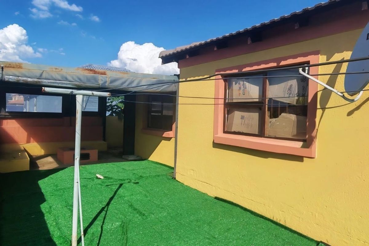 Rear exterior view featuring a covered patio area with built-in braai, artificial turf, and satellite dish installation.