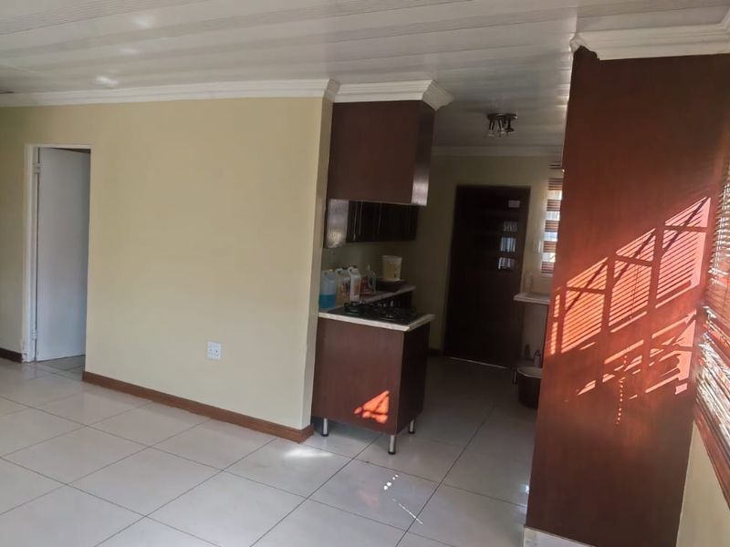 An open-plan living area featuring tiled flooring, cornicing, and a compact kitchen with built-in cabinetry, hob, and extractor fan.