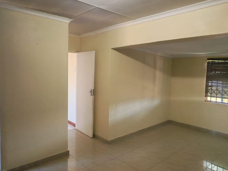 An empty bedroom featuring tiled flooring, an integrated shower area, and security window treatments, offering a blank canvas for renovation.