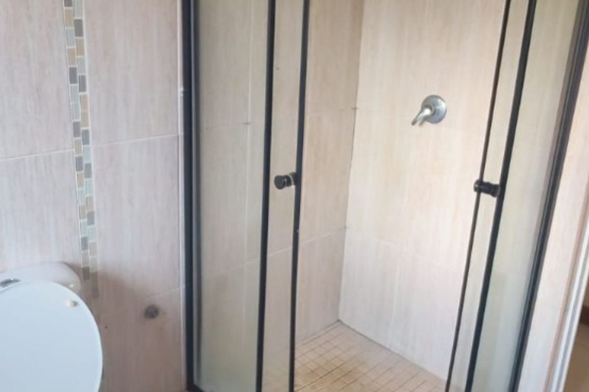 A functional bathroom featuring a corner shower enclosure with black framing, a standard toilet, and neutral wall and floor tiling.