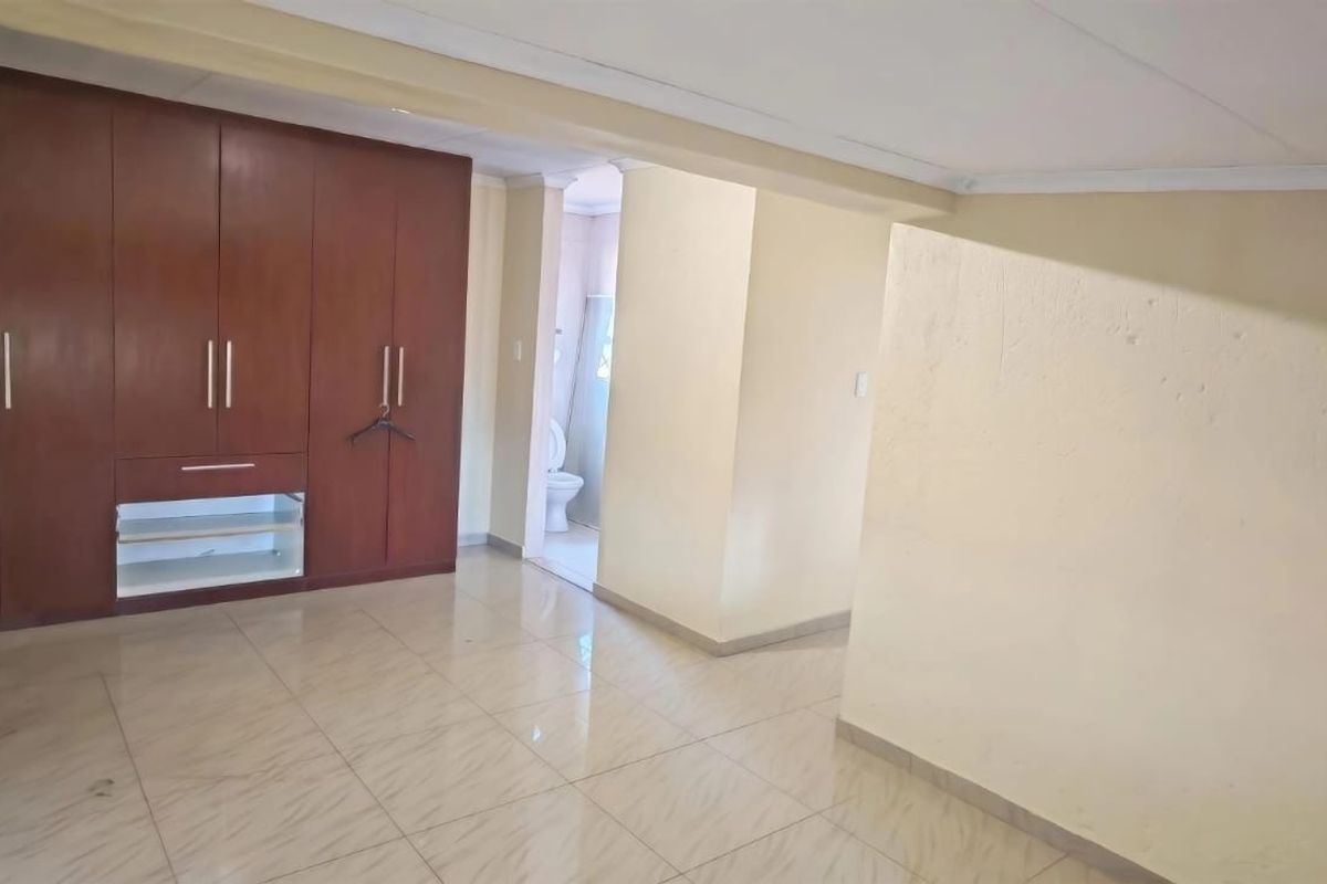 Spacious bedroom featuring built-in wooden cupboards, tiled flooring, and direct access to an en-suite bathroom.
