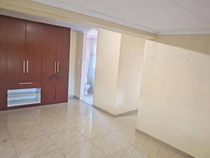 Spacious bedroom featuring built-in wooden cupboards, tiled flooring, and direct access to an en-suite bathroom.