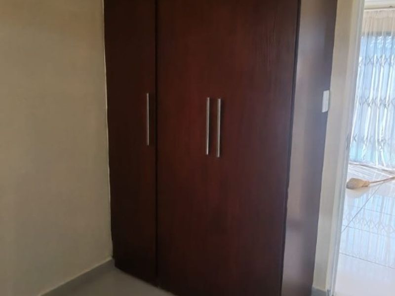 A bedroom featuring a dark wood built-in wardrobe and neutral tiled flooring, offering a clean and functional space.