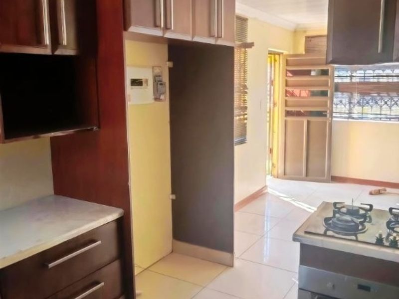 A functional kitchen featuring dark wood cabinetry, a gas stove with oven, and tiled flooring, leading towards an exterior doorway.