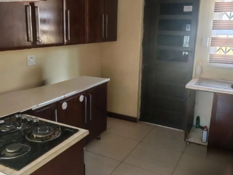 A functional kitchen featuring dark wood cabinetry, a gas hob, tiled flooring, and a rear access door.