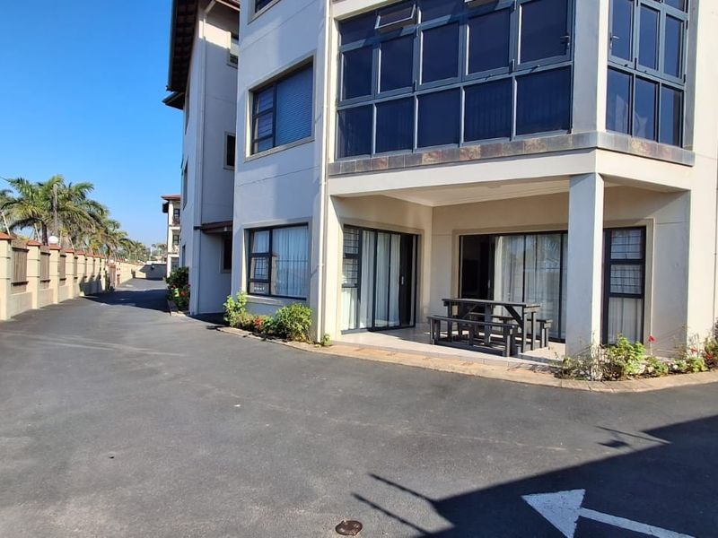 Exterior view of a multi-story residential building featuring a paved driveway, covered patio area, and secure perimeter fencing.