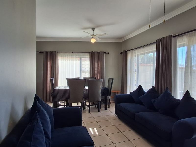 Open-plan living and dining area featuring tiled flooring, crown molding, a ceiling fan, and large sliding glass doors providing natural light.