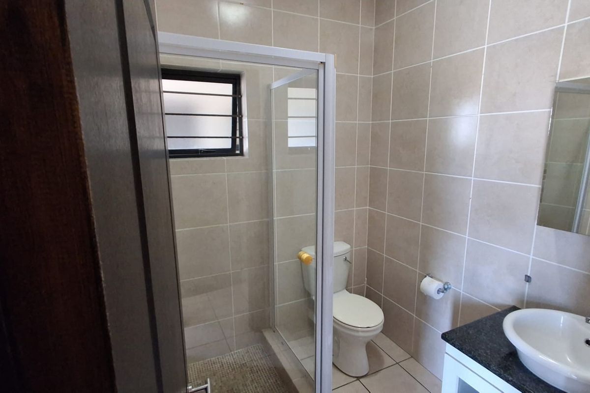 A clean and functional bathroom featuring a glass shower enclosure, a vanity with a basin, and neutral wall tiling.