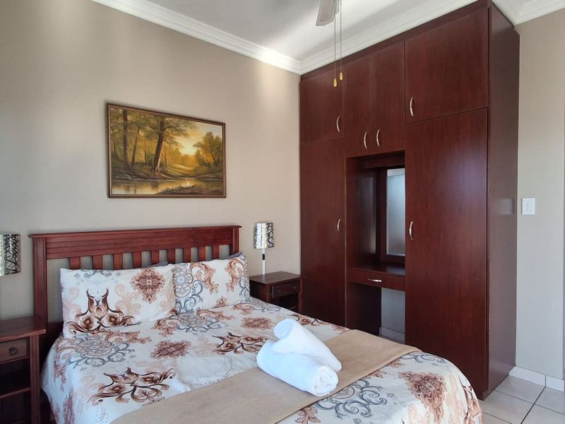 A well-maintained bedroom featuring dark wood built-in cupboards with an integrated vanity, crown molding, and neutral tiled flooring.