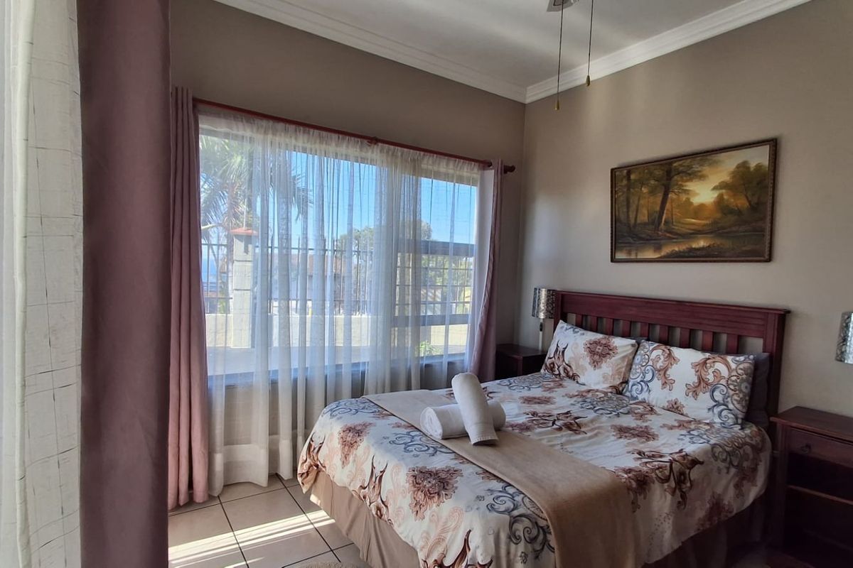 A well-lit bedroom featuring tiled flooring, neutral wall tones, and a large window allowing for natural light.