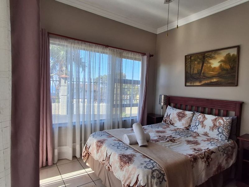 A well-lit bedroom featuring tiled flooring, neutral wall tones, and a large window allowing for natural light.