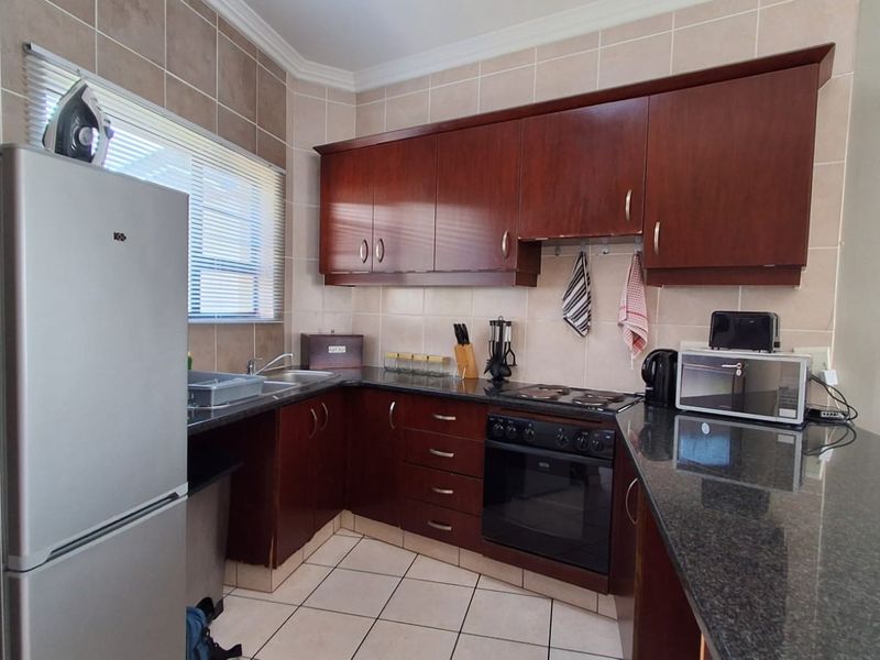 A functional kitchen featuring dark wood cabinetry, granite countertops, an electric hob, built-in oven, and tiled finishes throughout.