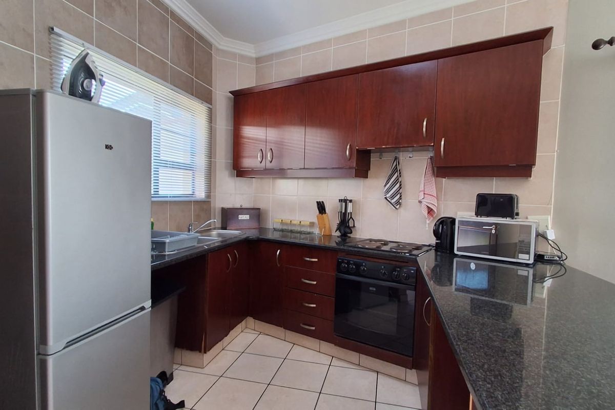 A functional kitchen featuring dark wood cabinetry, granite countertops, an electric hob, built-in oven, and tiled finishes throughout.