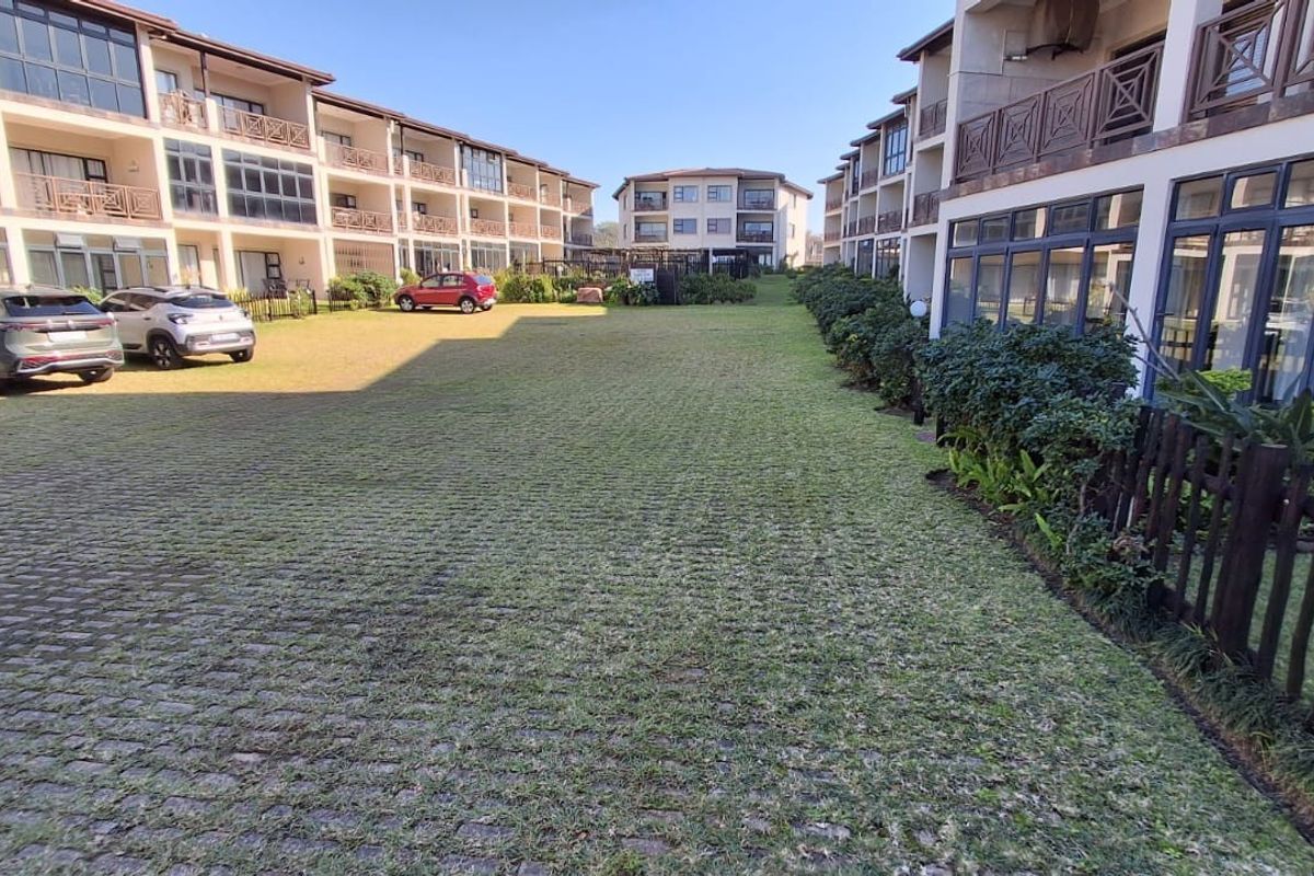 A view of the rear exterior area featuring a paved driveway, landscaped garden, and multi-story residential building facades with balconies.