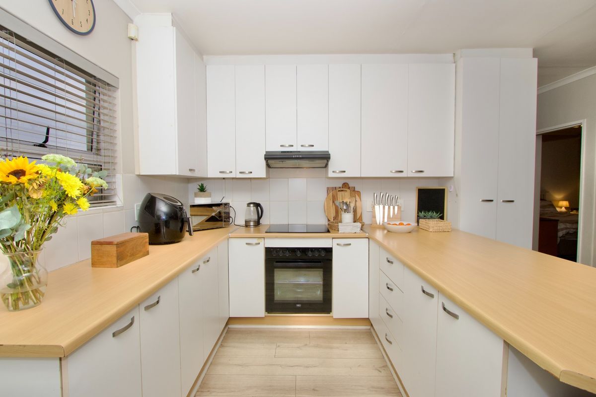 A well-maintained kitchen featuring white cabinetry, light wood-look countertops, a built-in oven, and an electric hob with an extractor fan.