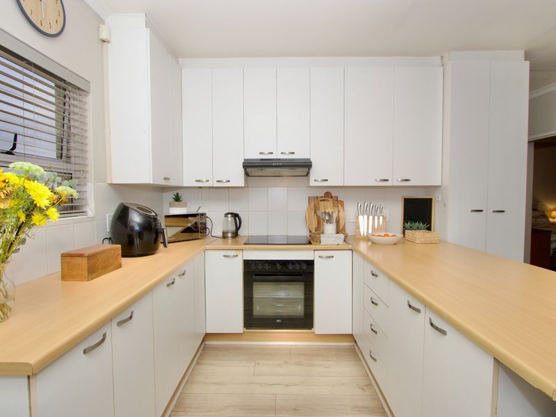 A well-maintained kitchen featuring white cabinetry, light wood-look countertops, a built-in oven, and an electric hob with an extractor fan.